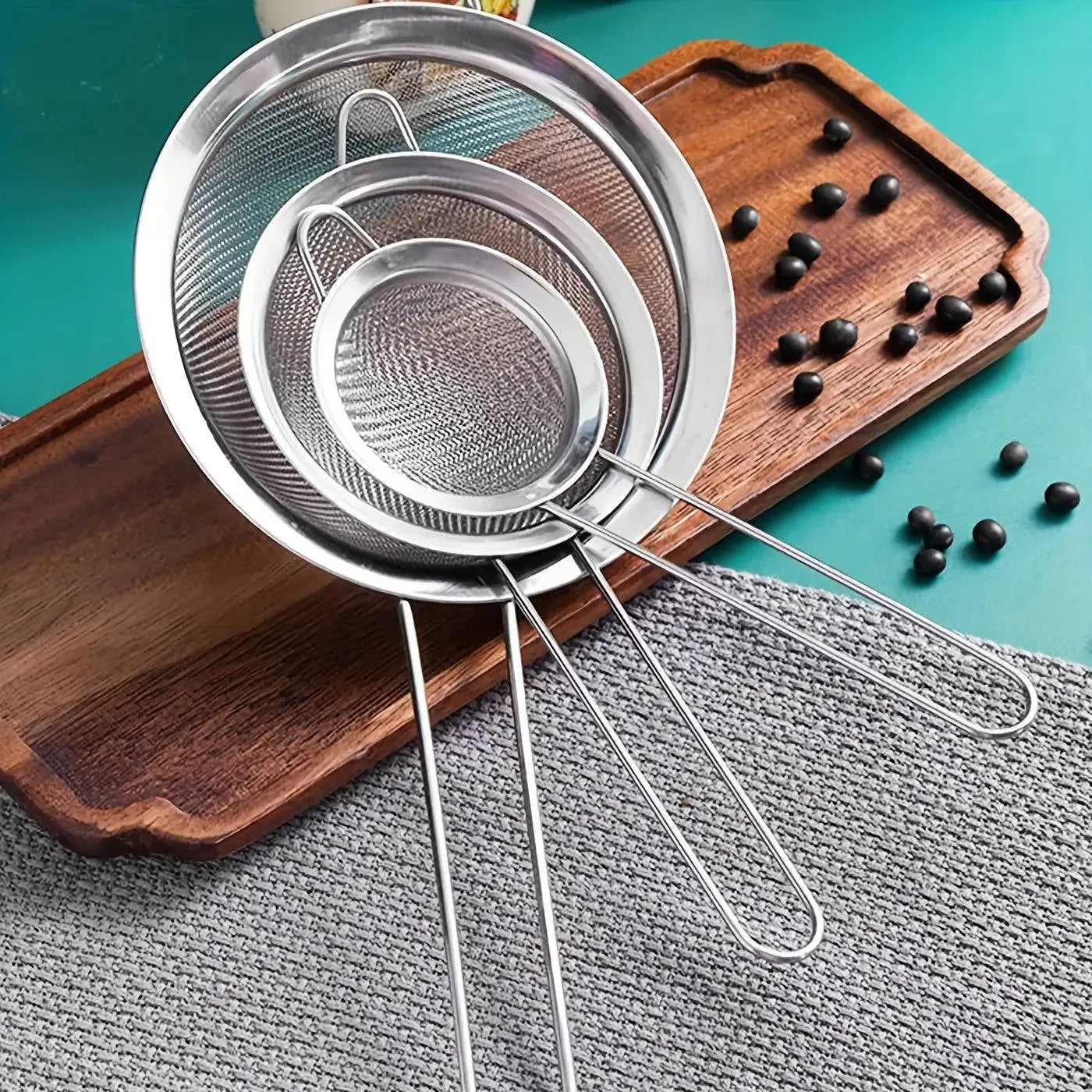 Three-piece Stainless Steel Strainer Set with fine mesh, stacked on a wooden board, essential kitchen tools for versatile straining tasks.