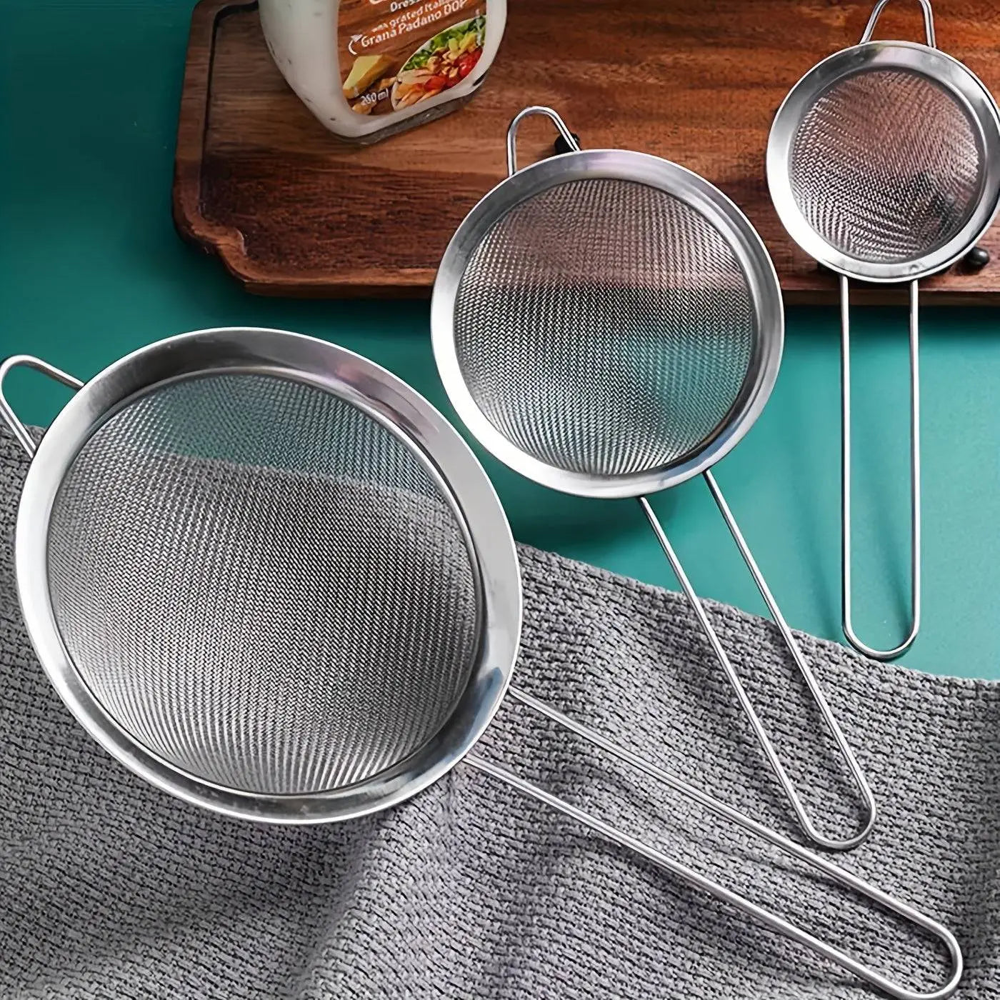 Stainless Steel Strainer Set with fine mesh, durable kitchen tools for straining tea, eggs, and vegetables, displayed on a green surface.