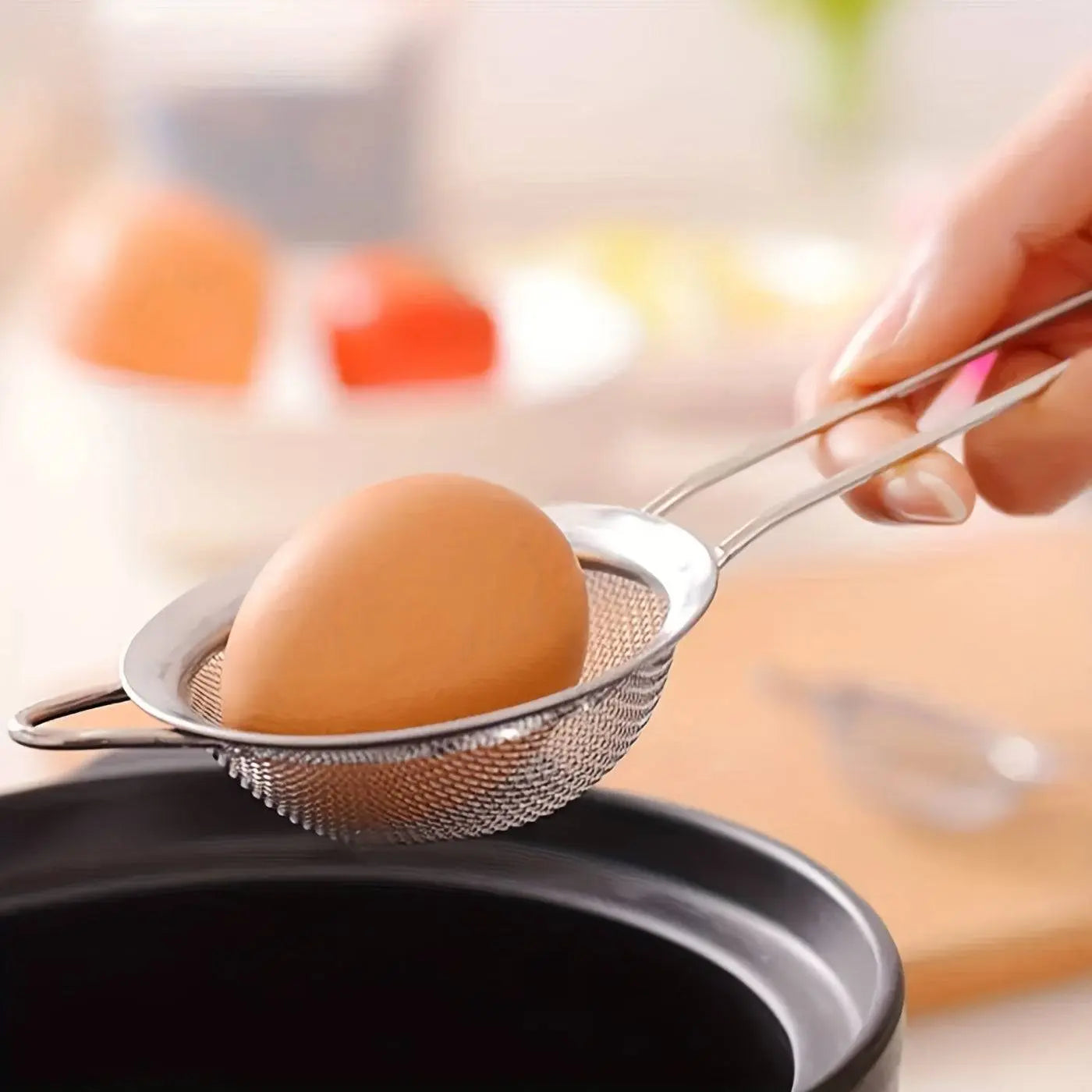 Small Stainless Steel Strainer from the set holding a boiled egg, showcasing fine mesh durability for kitchen straining tasks.