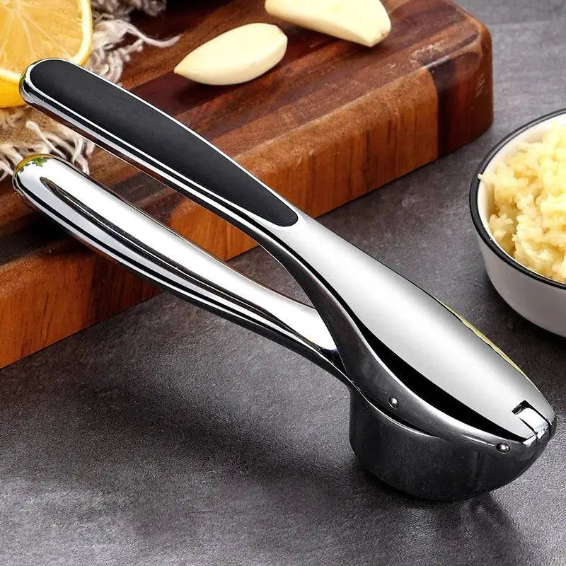 Closed Stainless Steel Garlic Masher - Manual Garlic Crusher with black grip, placed on kitchen counter near minced garlic and lemon.