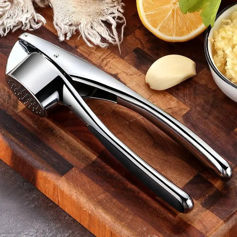 Stainless Steel Garlic Masher - Manual Garlic Crusher resting on a wooden board with garlic cloves and minced garlic bowl nearby.