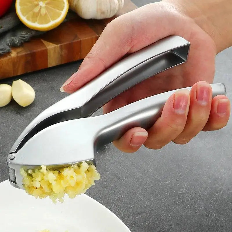 Hand using Stainless Steel Garlic Masher - Manual Garlic Crusher to press fresh garlic over a white plate, durable kitchen tool for mess-free prep.