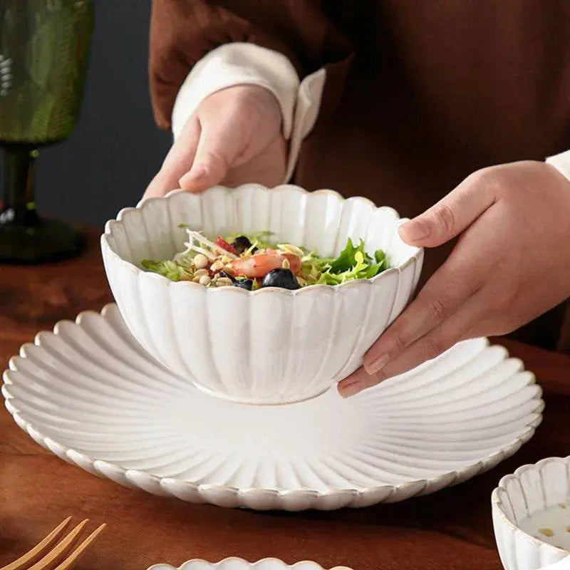 Hand holding a white ceramic bowl filled with salad over a matching plate, showcasing the durable and elegant ceramic tableware set.