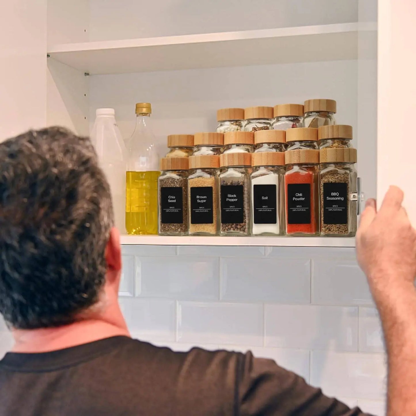 Glass Spice Jar Set with Bamboo Lids | Airtight, Clear Design neatly organized on a kitchen shelf, with a man reaching for a jar among oils and condiments.