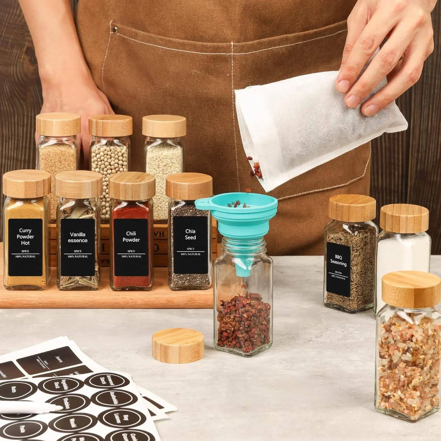 Glass Spice Jar Set with Bamboo Lids | Airtight, Clear Design showing a person filling a spice jar using a funnel, surrounded by labeled jars and sticker sheets.