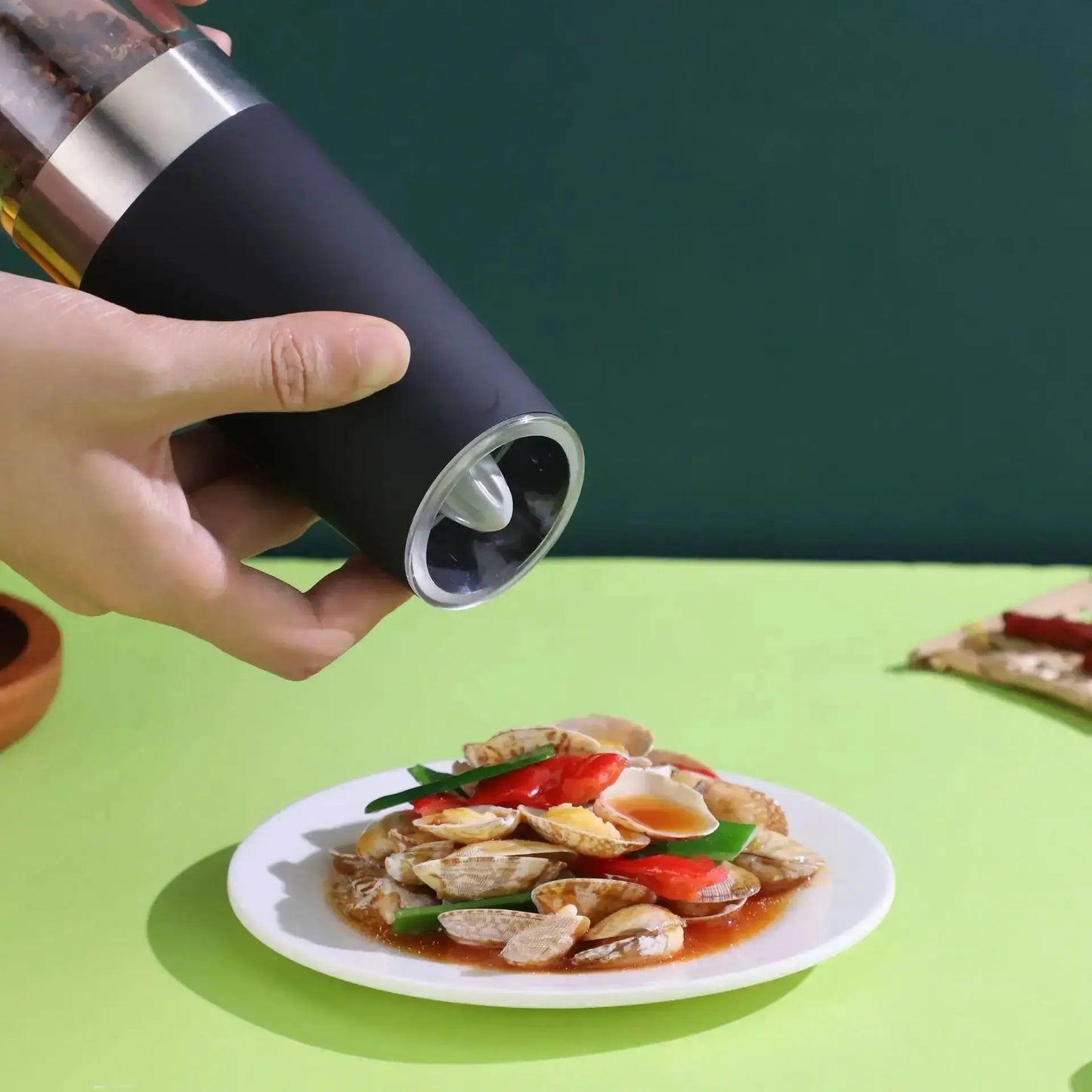 Hand using Automatic Pepper Grinder - Electric Grinder to season a plate of food, showcasing easy one-touch operation and modern design.