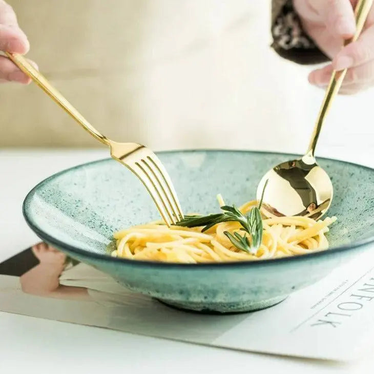 Using the 24-piece golden cutlery set to serve spaghetti in a green bowl, ideal for elegant holiday dinners.