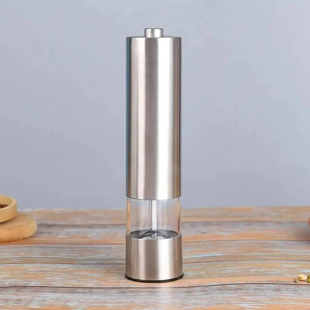 Electric Grinder for Salt & Pepper standing upright on a wooden surface, showcasing its stainless steel body and transparent spice chamber.